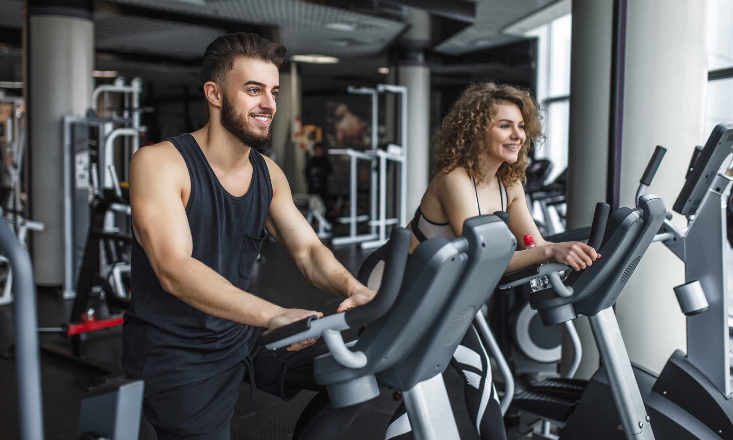 Attractive young woman and her trainer running on treadmill in gym. Slim girl jogging in fitness club, smiling at camera. Healthy lifestyle concept, cardio training.
